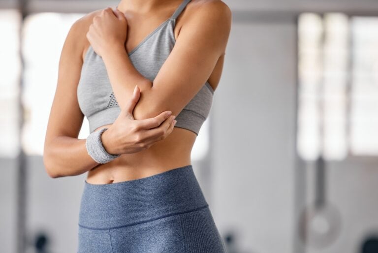 woman in gray sportswear holding her elbow