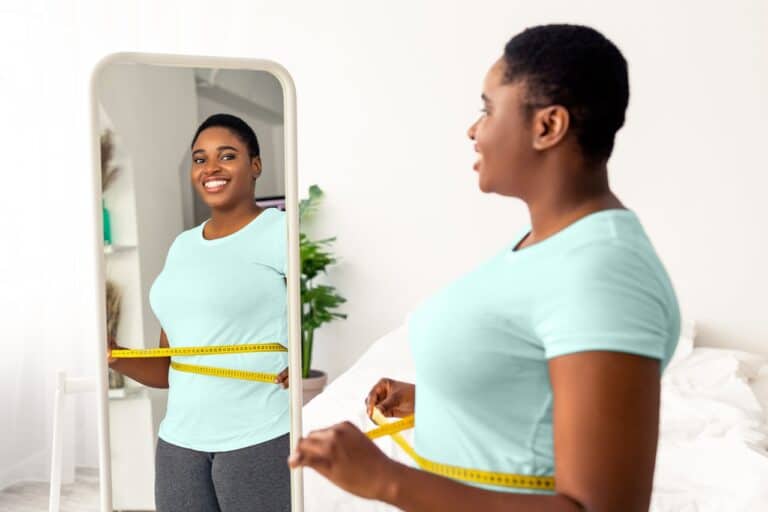 woman measuring waist in mirror